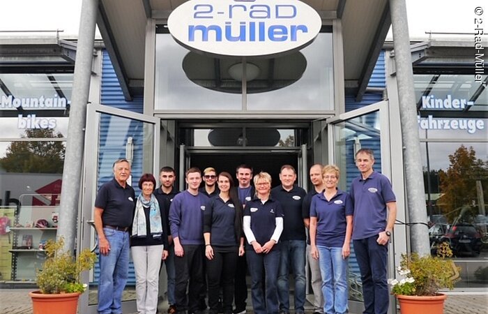 Die Mitarbeiter von 2-Rad Müller stehen vor dem überdachten Eingang des Geschäfts.