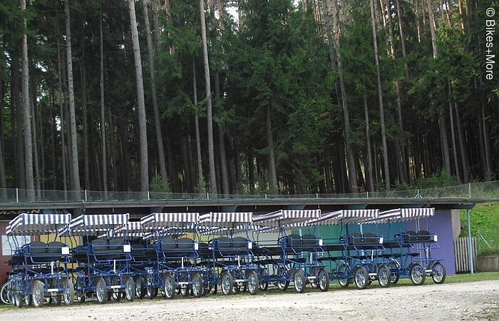 Rikschazentrum Pleinfeld Sechs Rikschas stehen in einer Reihe auf einem Schotterplatz. Im Hintergund Wald.