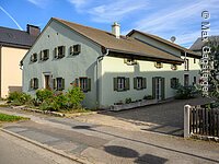 Jurahaus in Dettenheim, an der Hauptstraße gelegen, das Haus hat einen grünen Anstrich und Holzfensterläden, an der Stirnseite des Hauses befinden sich einige Sträucher