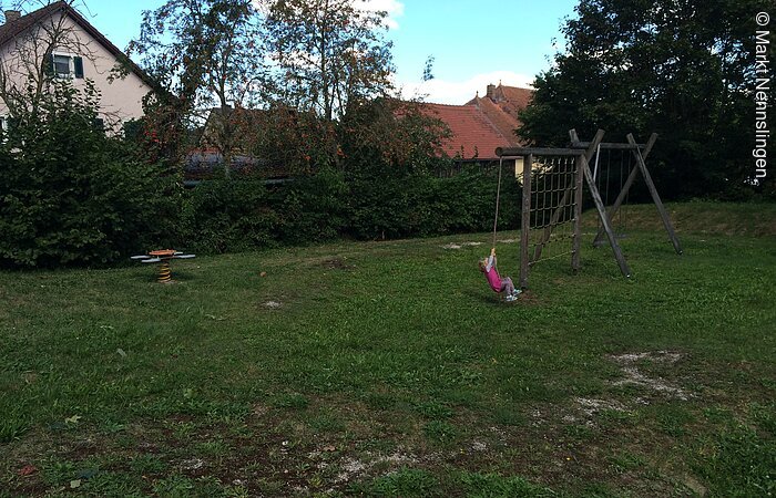 Spielplatz in Nennslingen - Weißenburger Straße Mädchen sitzt auf Schaukel mit runder Sitzfläche.