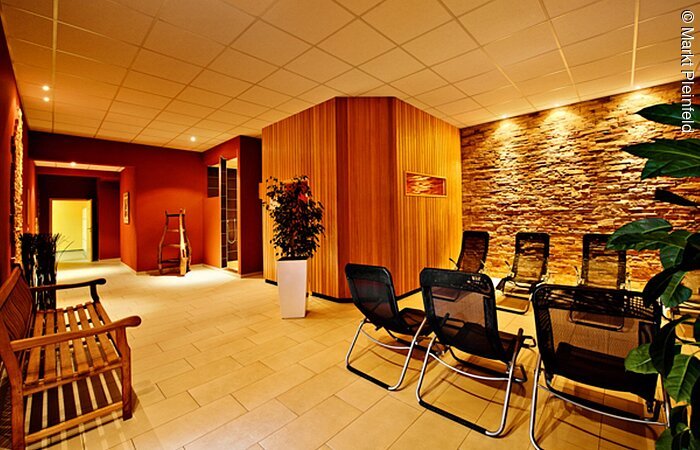 Wellnessbereich Ein in warmes Licht getauchter Wellnessbereich mit Liegen und Bank zum entspannen. Rostrote Wand mit weißer Decke und weißem Boden.