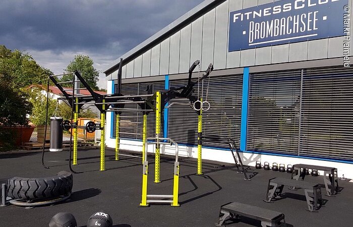Fitness Club Brombachsee Fitnessgeräte im Freien. Dahinter ein Gebäude mit einem Schild: Fitness Club Brombachsee