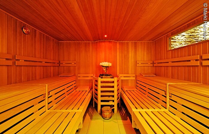 Entspannung in der Sauna Innenraum einer Holzsauna. In der Mitte der Aufguß. Rechts und links Bänke aus Holz. Die Sauna ist erleuchtet von oragenem Licht.