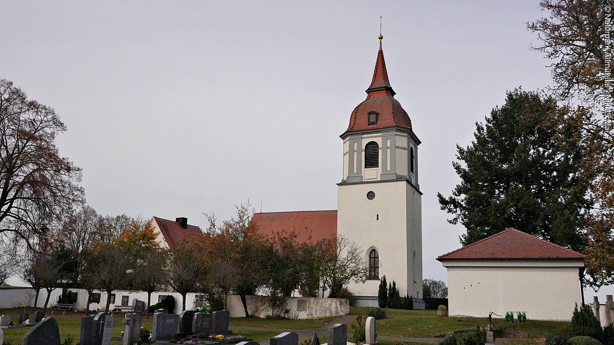 Gunzenhausen St. Michael Außenansicht mit Friedhof Kirche mit Turm und rotem Dach in einem Friedhof mit Grabsteinen und Bäumen bei bewölktem Himmel.