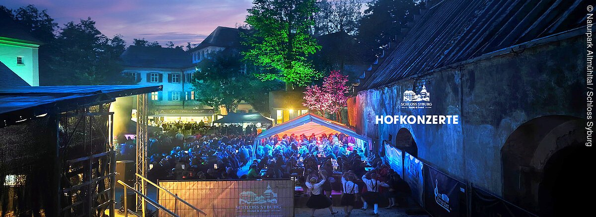 Abendliche Außenaufnahme eines beleuchteten Konzertpublikums bei den Hofkonzerten im Schloss Syburg.